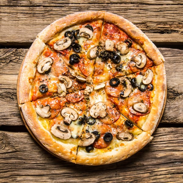 A sliced pizza with mushrooms, black olives, and pepperoni on a rustic wooden table.