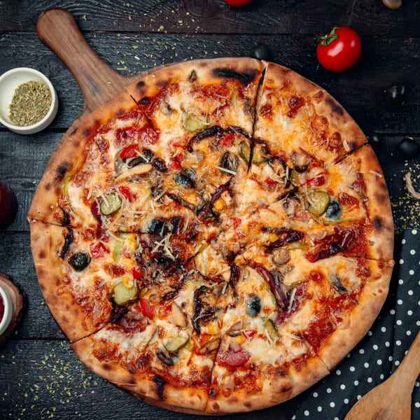 A freshly baked, sliced pizza with various toppings, including olives, peppers, and mushrooms, on a wooden board.