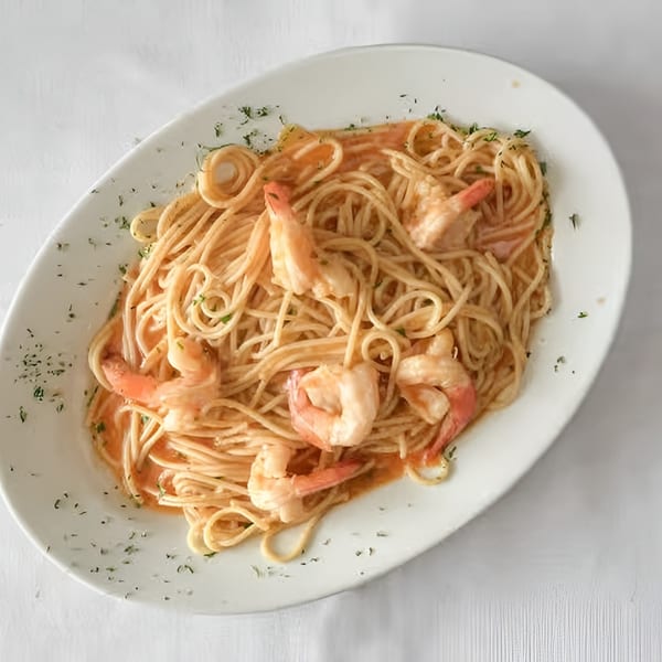Spaghetti with shrimp and a creamy orange sauce, garnished with herbs on a white oval plate.