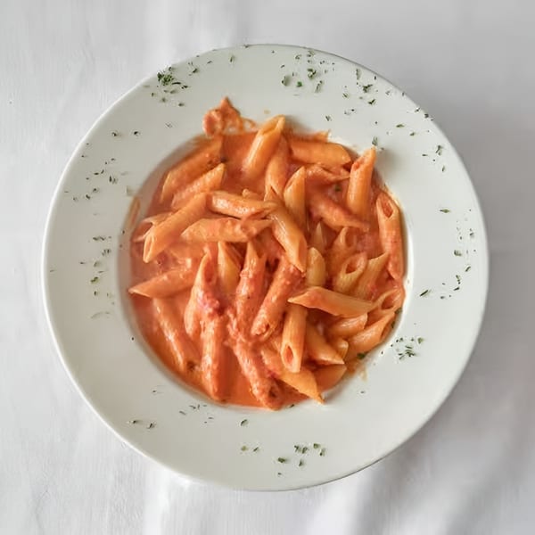 Penne pasta in a creamy red sauce, garnished with herbs, served on a white plate.