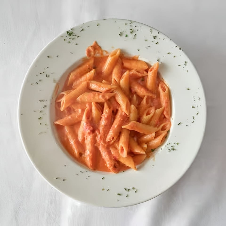 Penne pasta in a creamy red sauce, garnished with herbs, served on a white plate.