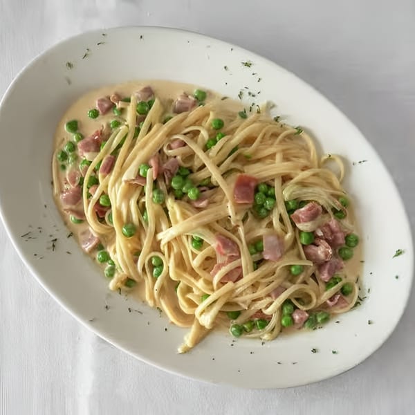 Creamy pasta with peas and ham on a white oval plate, garnished with herbs.