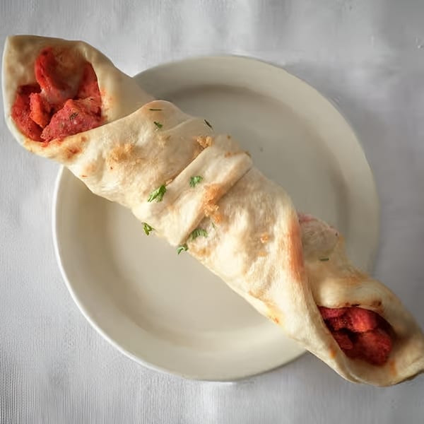 A chicken tikka roll, a popular Indian street food, on a white plate.